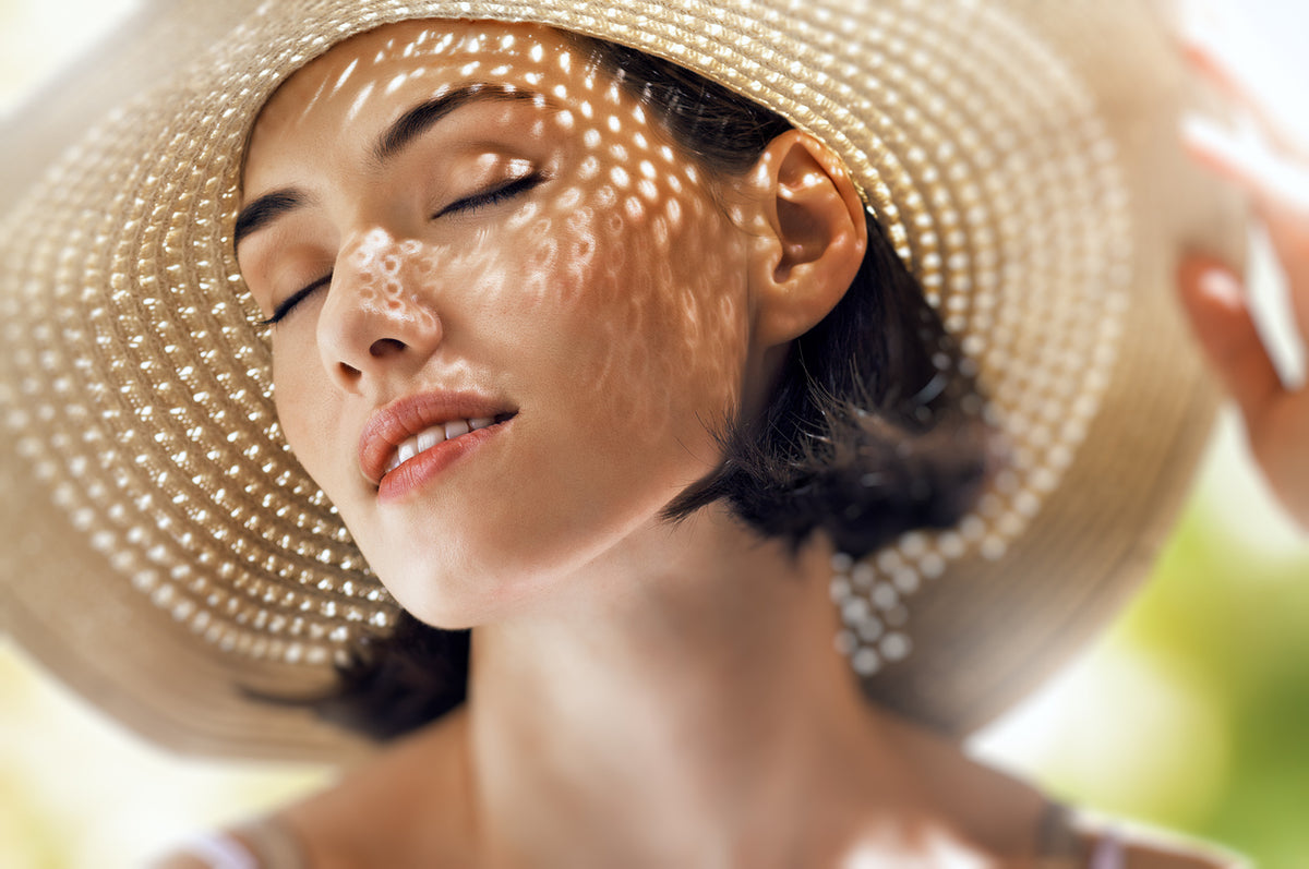 Woman in a wide-brimmed sun hat with sunlight on her face – summer skincare routine